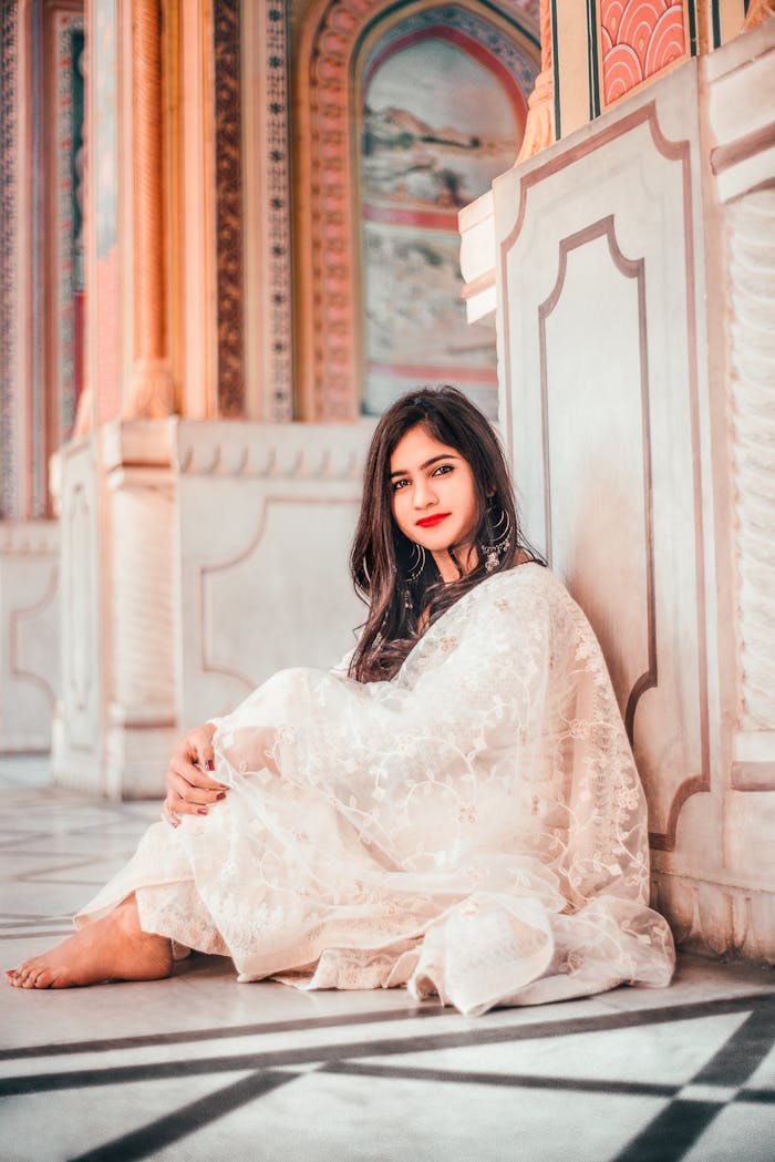 Young woman in traditional Indian outfit with red lipstick, sitting indoors in Jaipur's architectural setting.